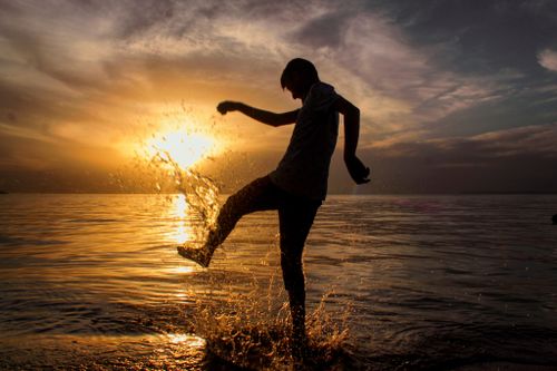 Free A silhouette of a man kicking water at sunset on a beach in Van, Turkey. Stock Photo