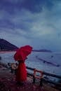 雨天，海边站着一名身穿红色连衣裙、打着伞的女子