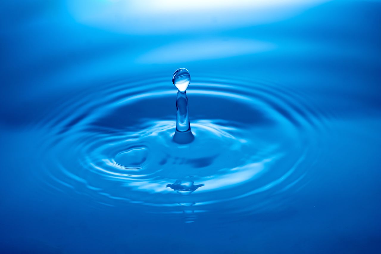 capture of a water droplet creating ripples on a blue surface showcasi