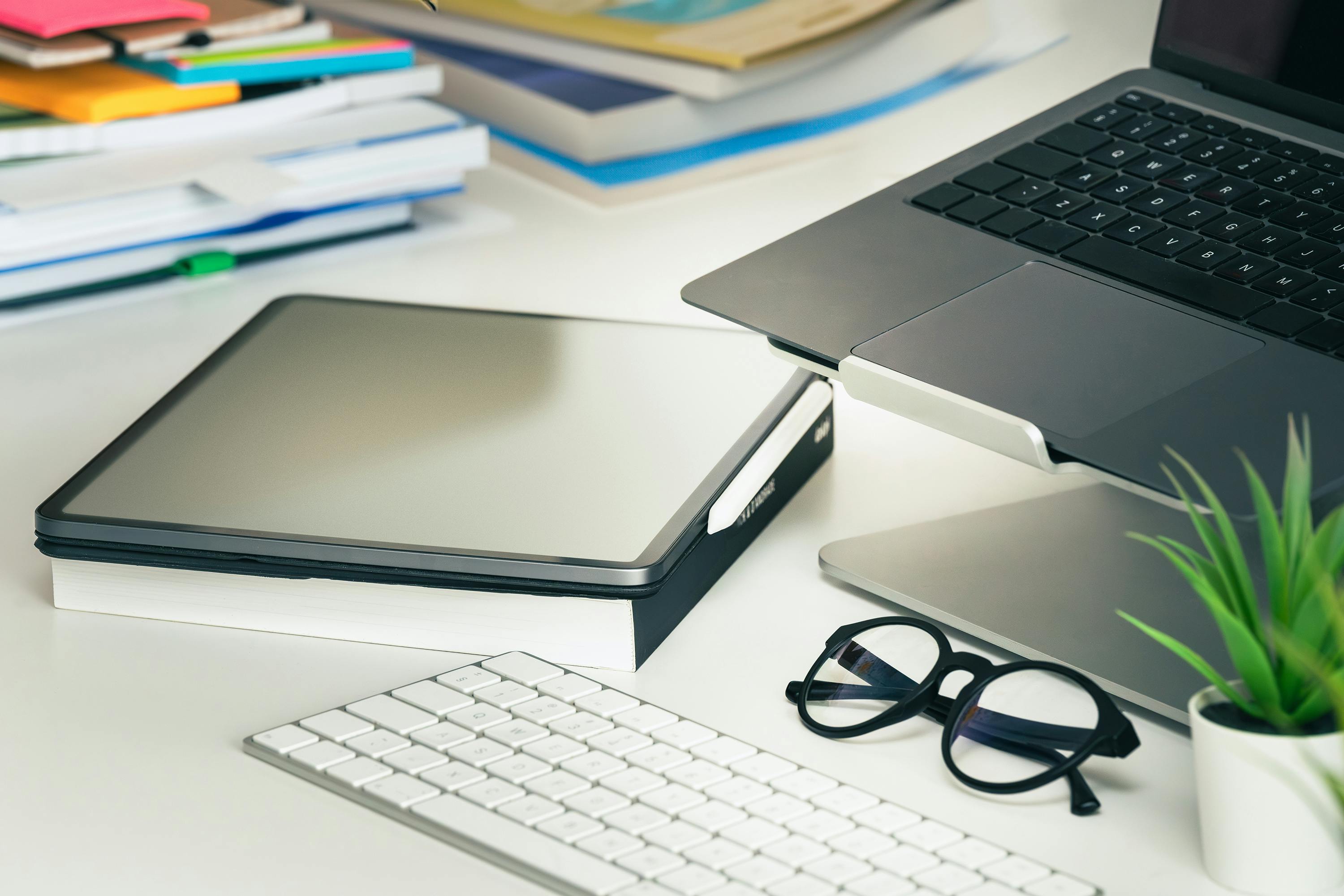 A sleek office setup featuring a laptop, tablet, eyeglasses, and keyboard on a tidy desk.