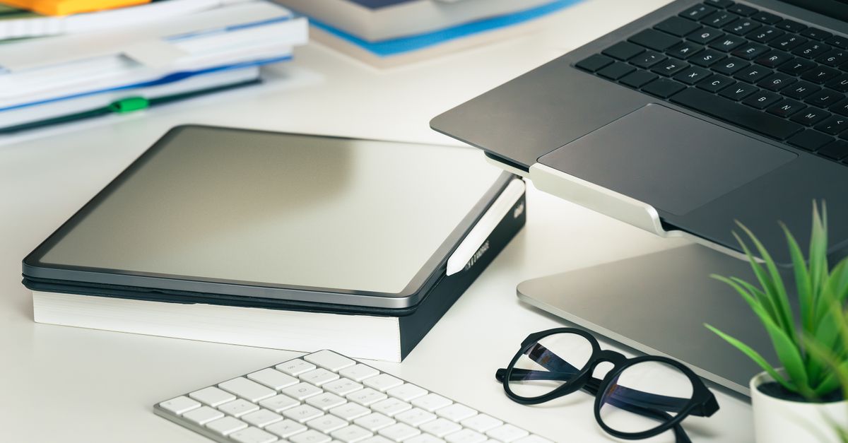 A sleek office setup featuring a laptop, tablet, eyeglasses, and keyboard on a tidy desk.