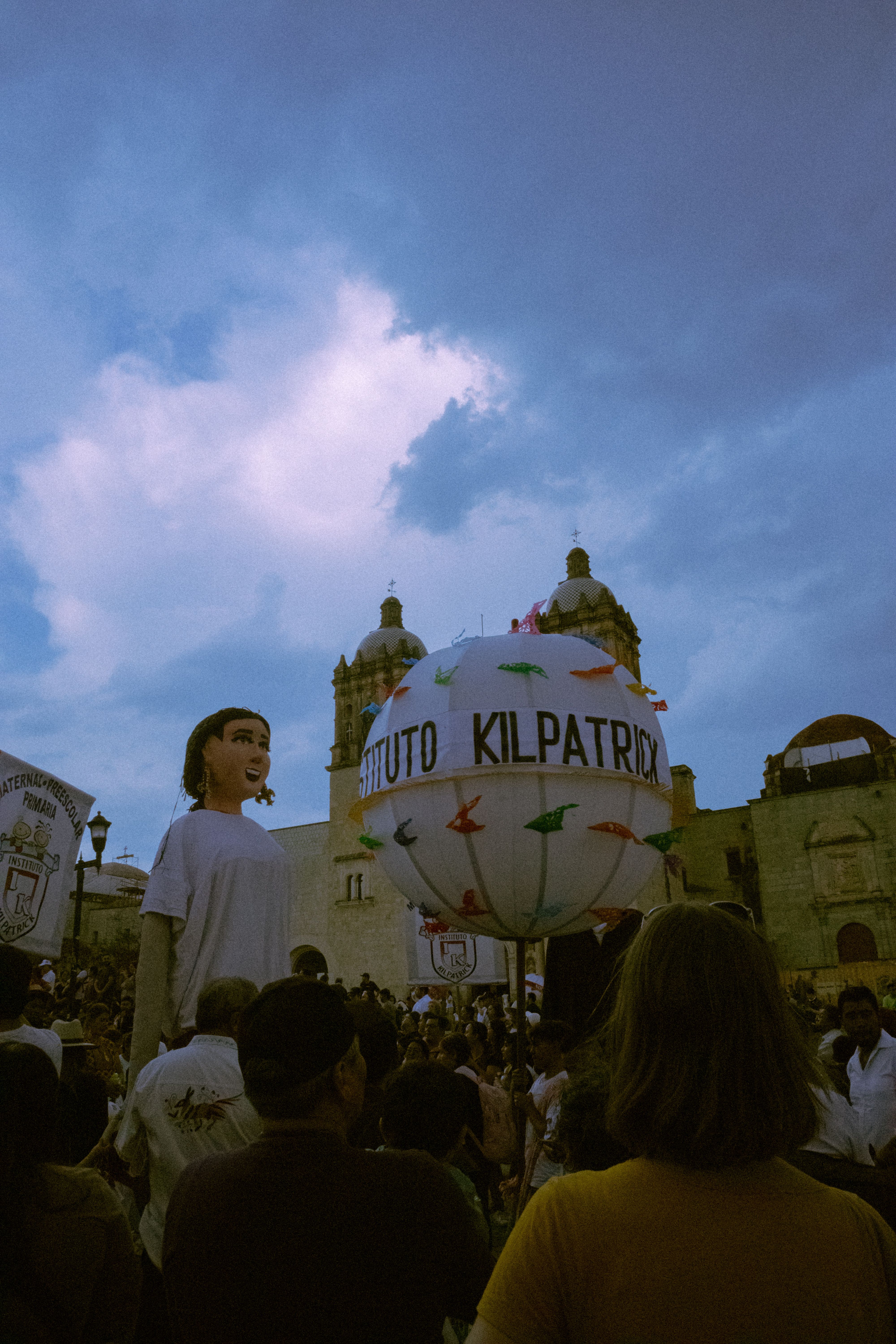 A vibrant parade with giant puppets and balloons in a historic city square during daytime.
