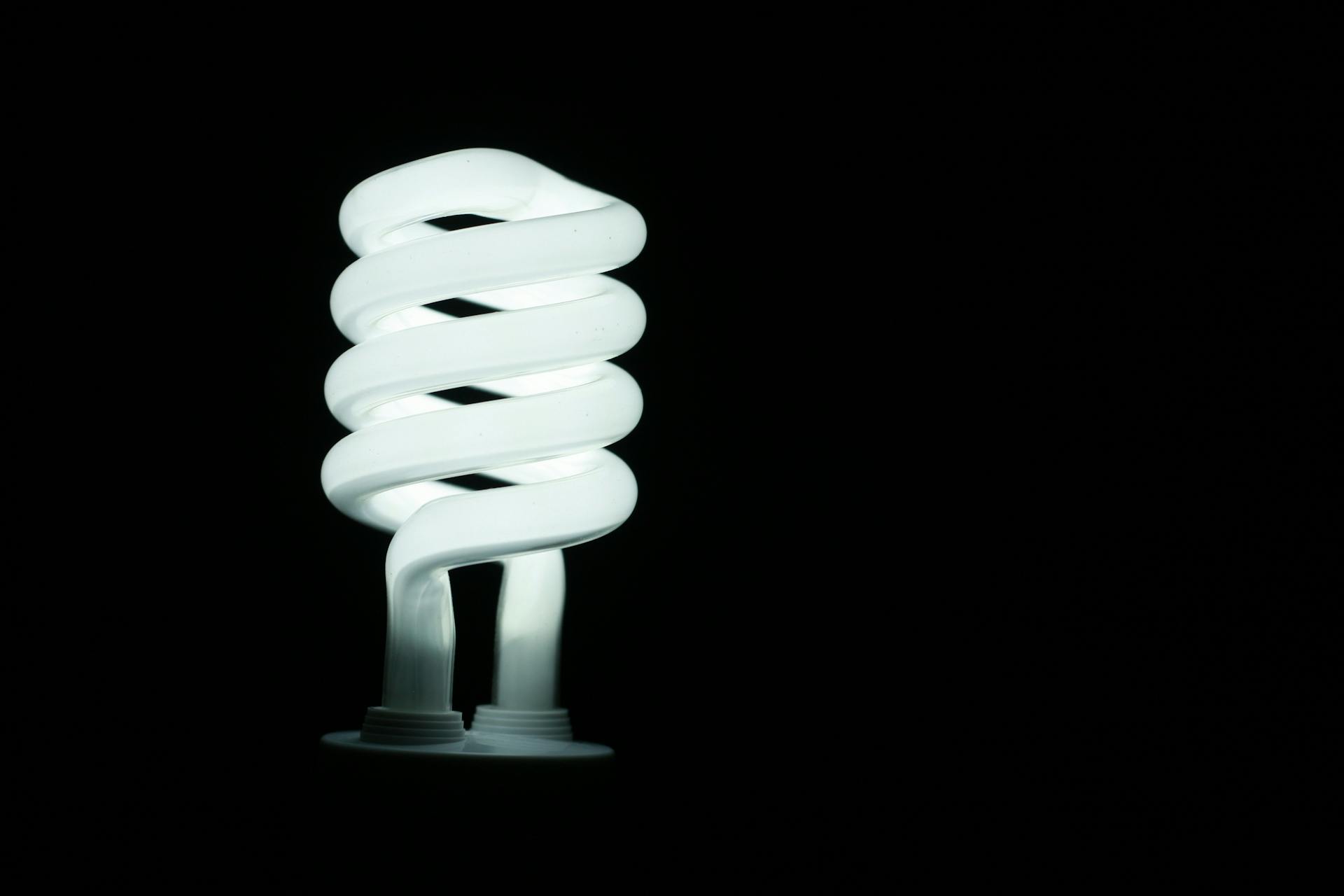 Illuminated spiral fluorescent light bulb glowing against a dark black background, showcasing energy efficiency and modern lighting design.