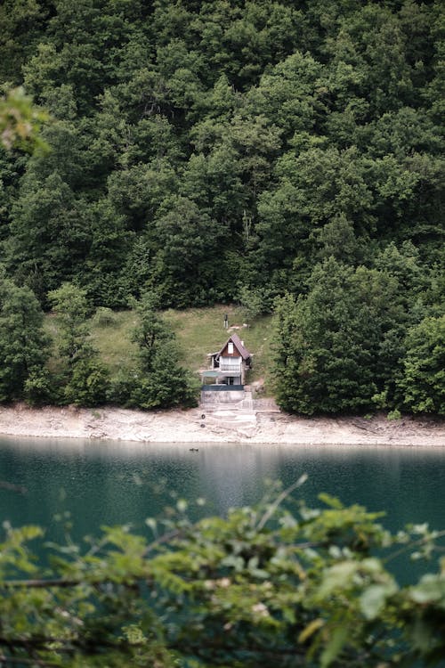 A small house sits on a hillside next to a lake