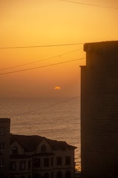 Golden sunset over ocean with urban silhouette and serene seaside view.