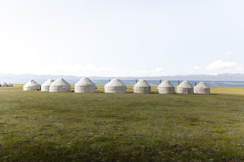 Free Traditional Mongolian yurts lined up on expansive green plains with mountains in the distance. Stock Photo