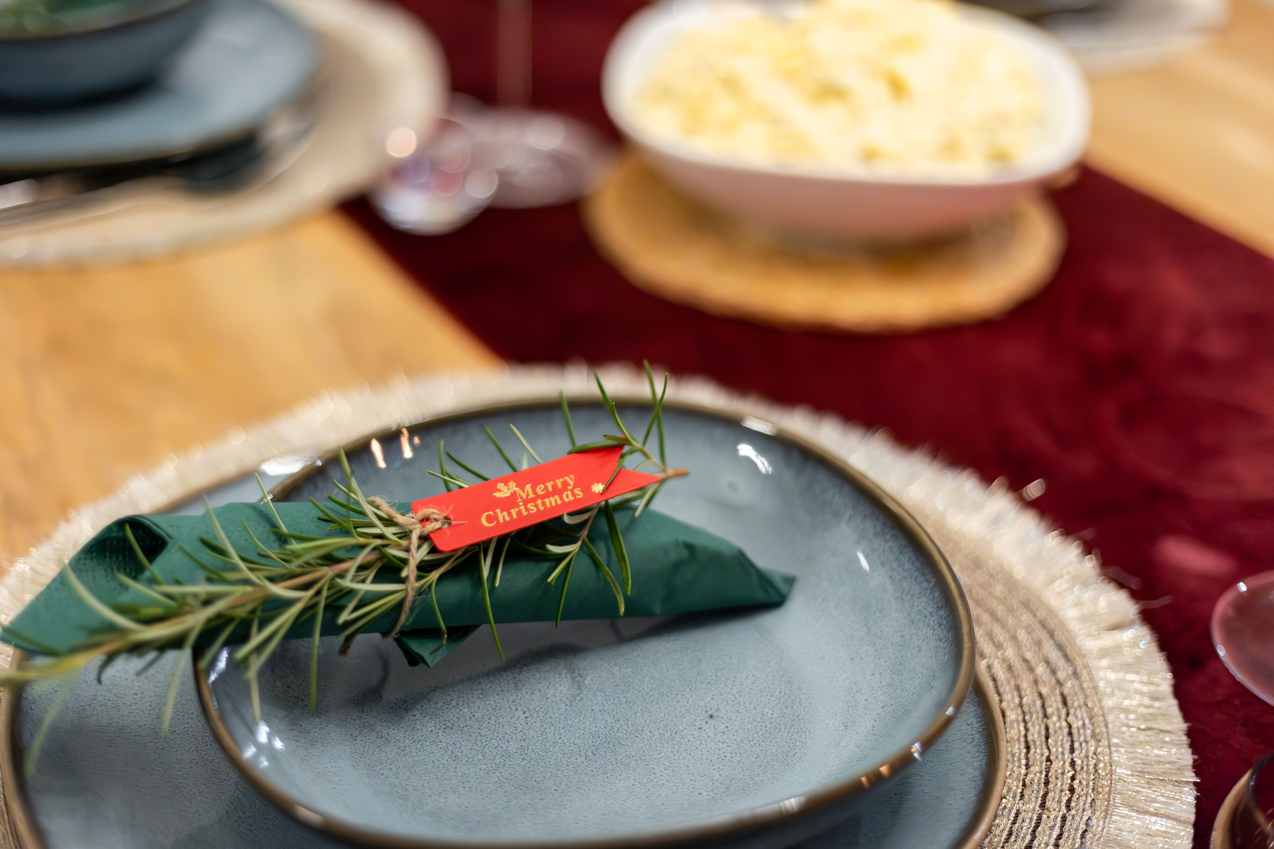 Mensagem de Natal em uma mesa de jantar decorada com prato, utensílios e um raminho de alecrim para uma celebração festiva.