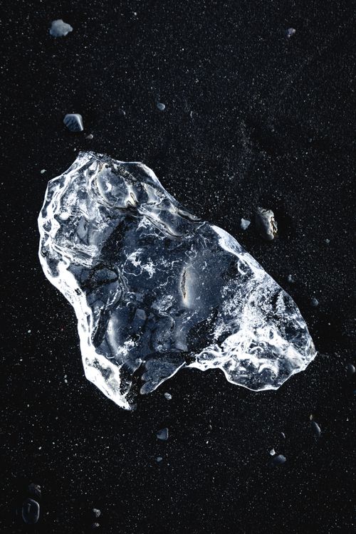 Free Striking close-up of a transparent ice fragment on black sand, highlighting nature's contrasts. Stock Photo