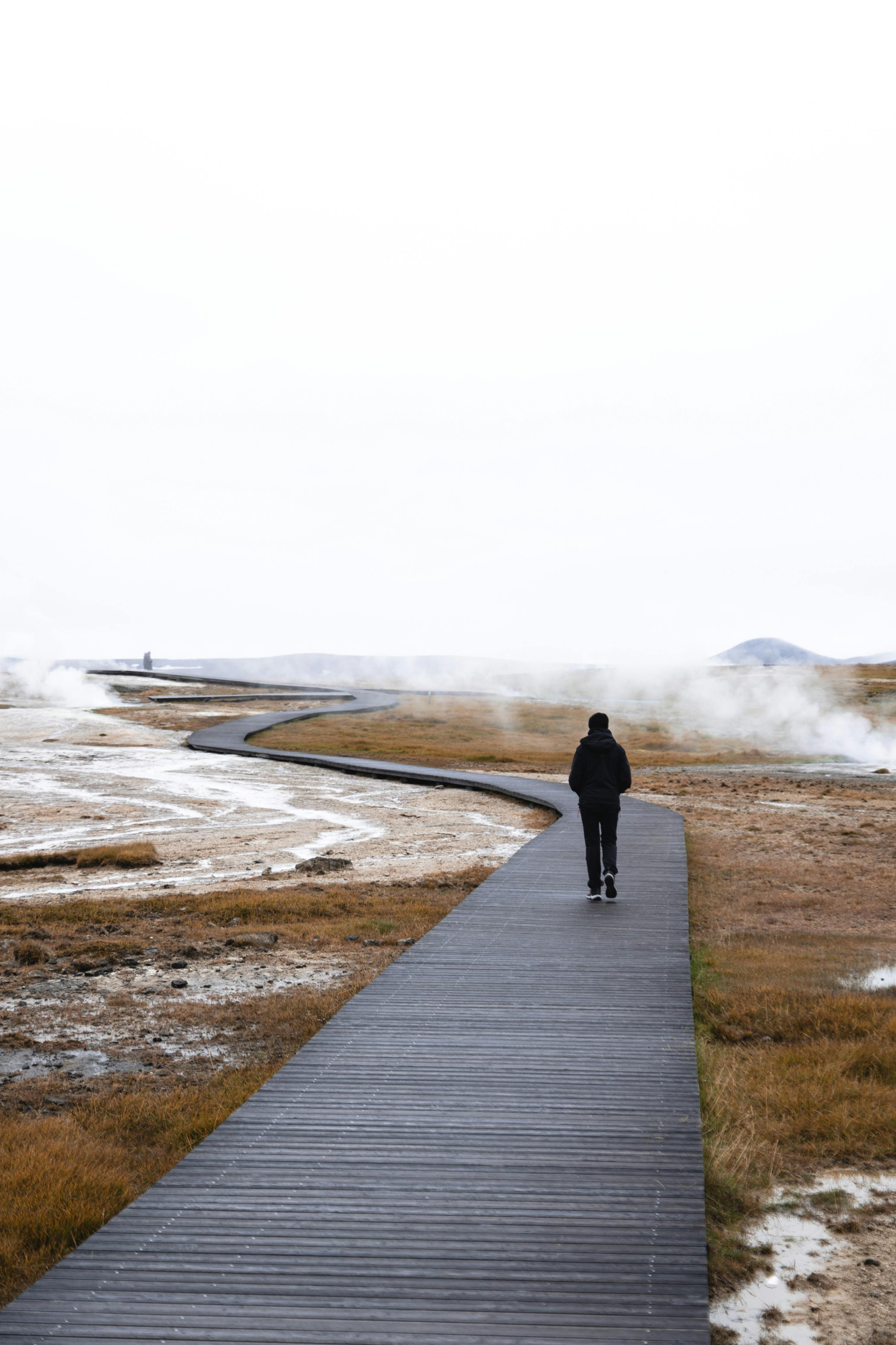 A person walking on a boardwalk in Iceland's wintry landscape with geothermal steam.