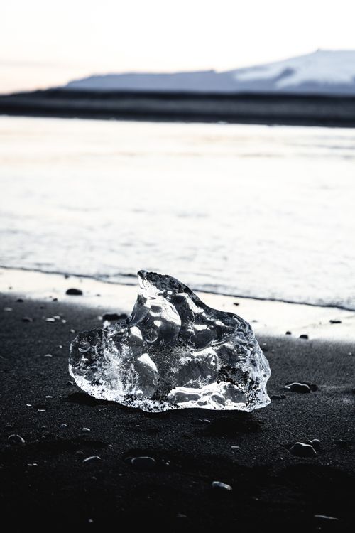 Free A clear ice chunk on a black sand beach in Iceland, showcasing nature's unique contrast. Stock Photo
