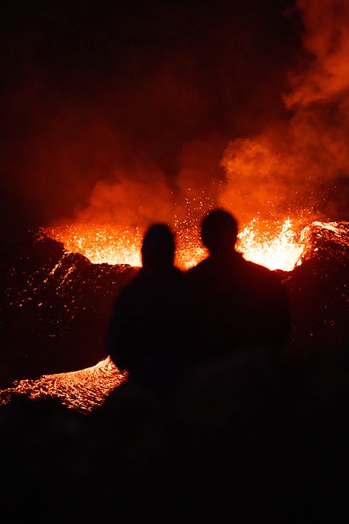 Two people are silhouetted against the glow of a lava flow