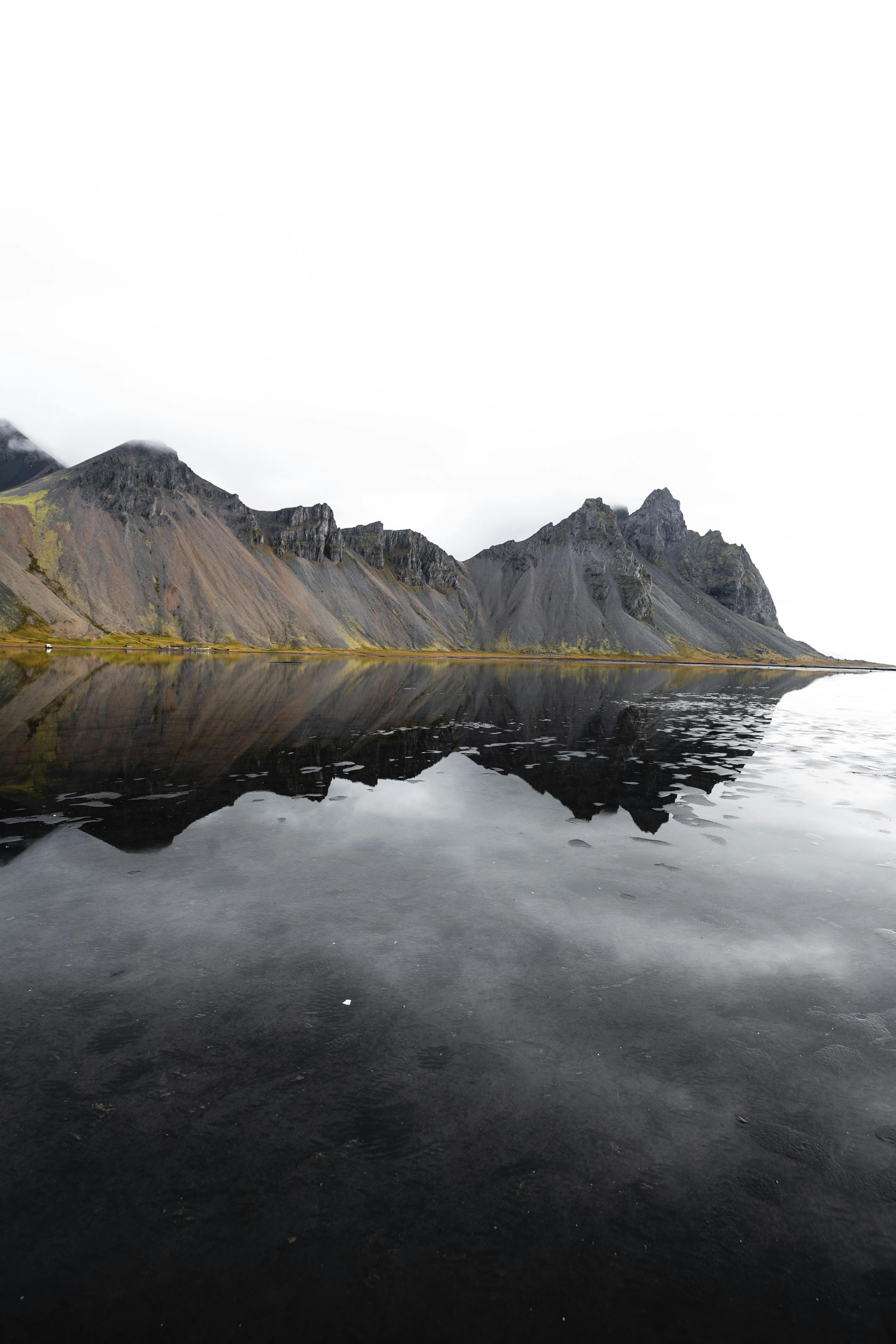 Stunning reflection of Vestrahorn mountain on a serene coast under a cloudy sky in Iceland.