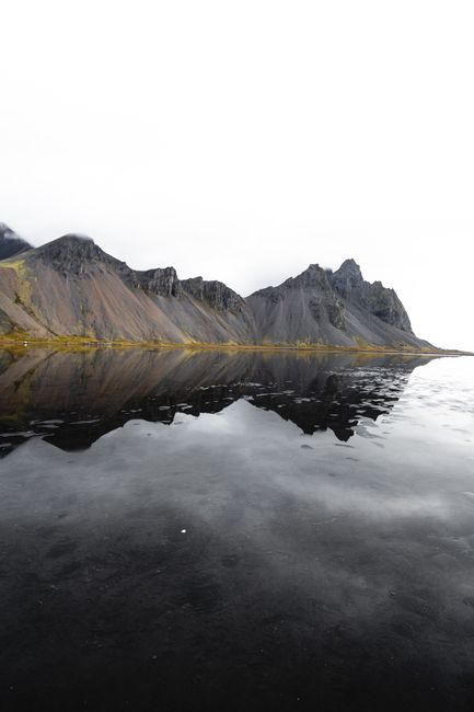 Stunning reflection of Vestrahorn mountain on a serene coast under a cloudy sky in Iceland.