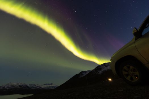 Explore the dazzling northern lights dancing over snowcapped peaks with a car in foreground, ideal for travel inspiration.