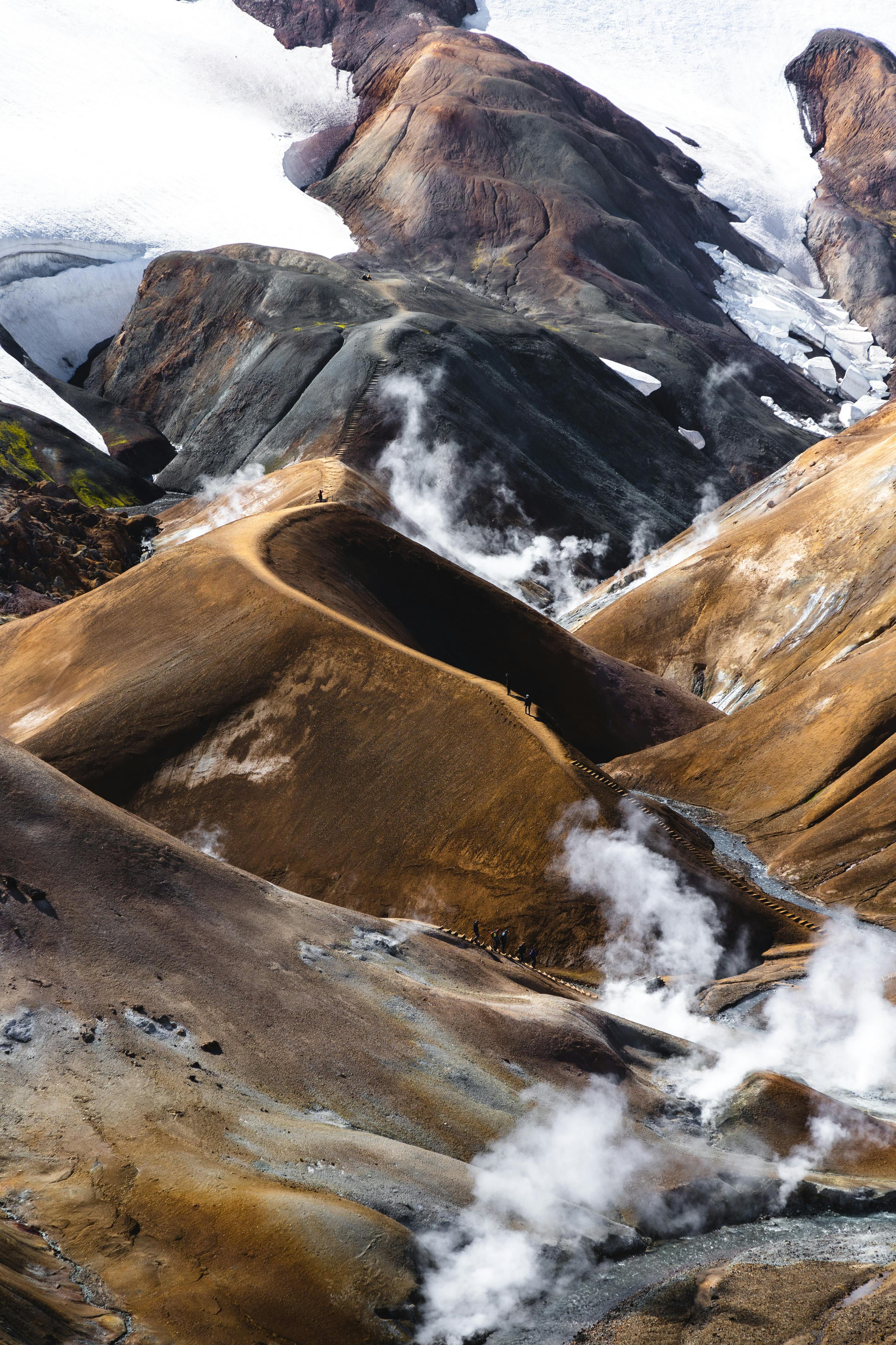 Stunning aerial view of steaming geothermal landscape with snow and rock formations.