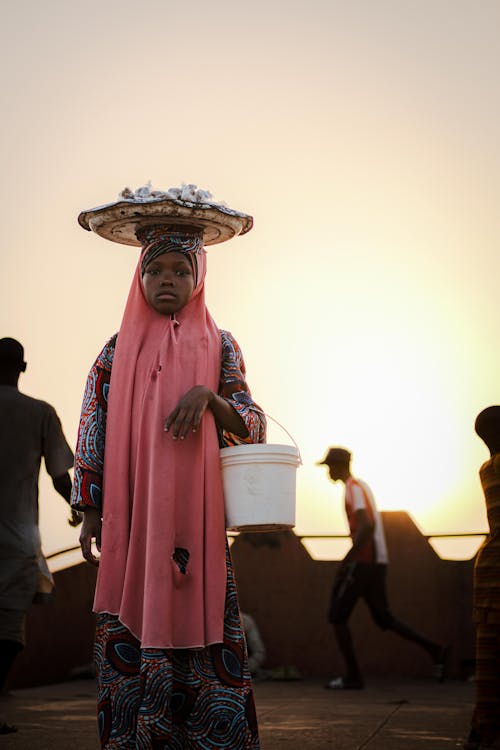 A woman in a pink headscarf carrying a bucket of water