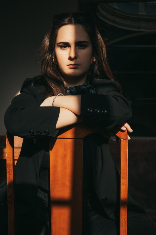 Free A young woman sits in sunlight, casting dramatic shadows for a moody effect. Stock Photo