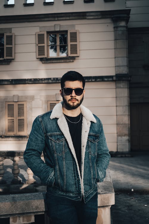 A man in a denim jacket and sunglasses standing in front of a building