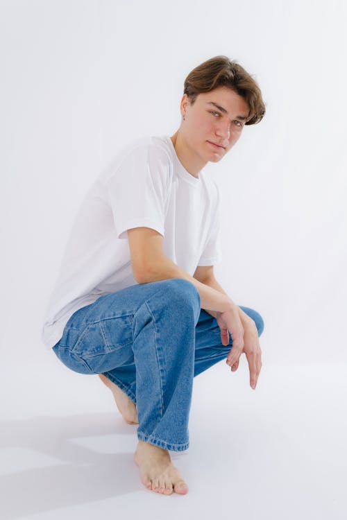 A young man in white shirt and blue jeans squatting