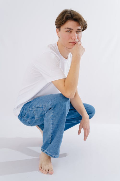 A young man in white shirt and blue jeans squatting