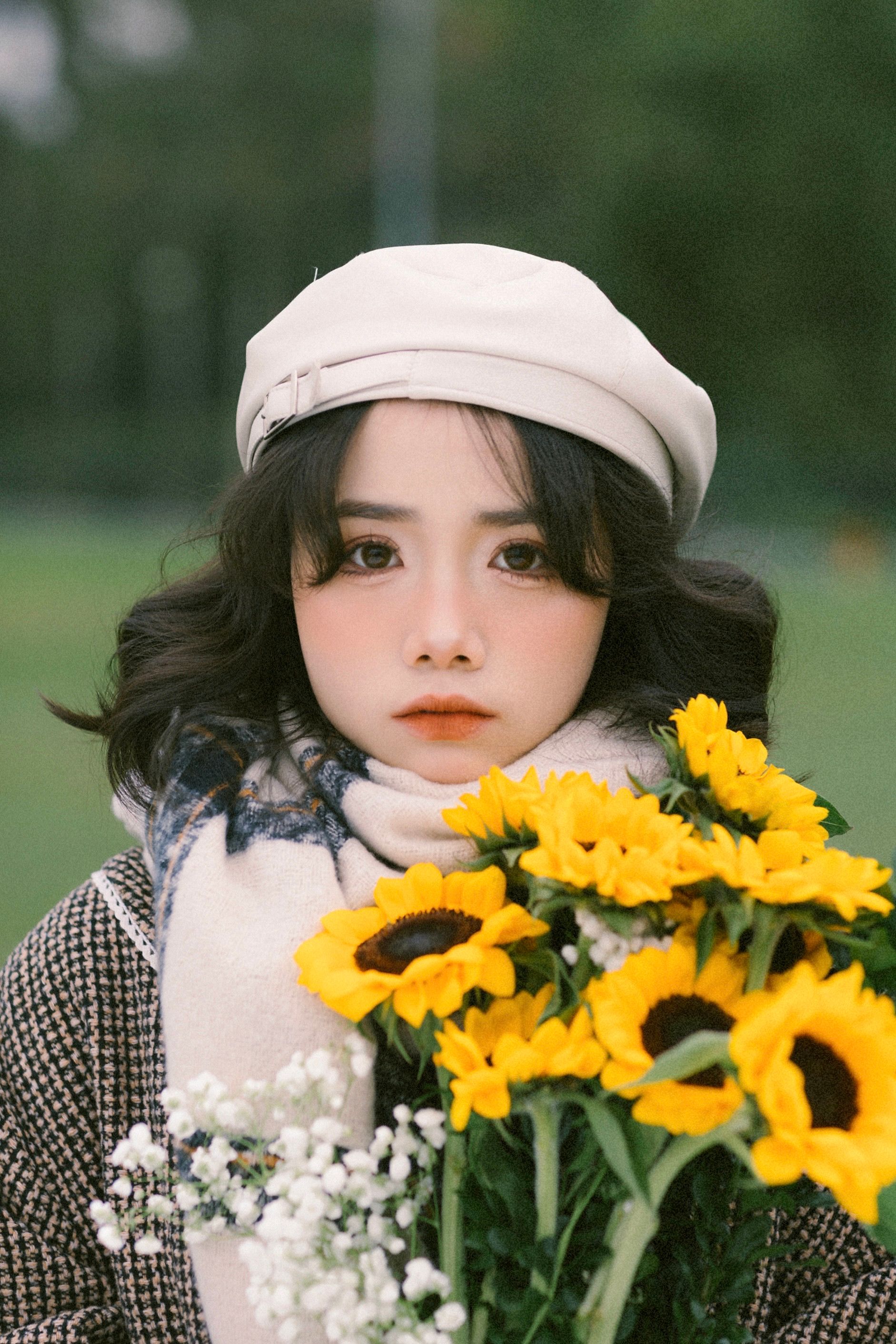 Portrait of a young woman in a beret holding a bouquet of sunflowers outdoors.