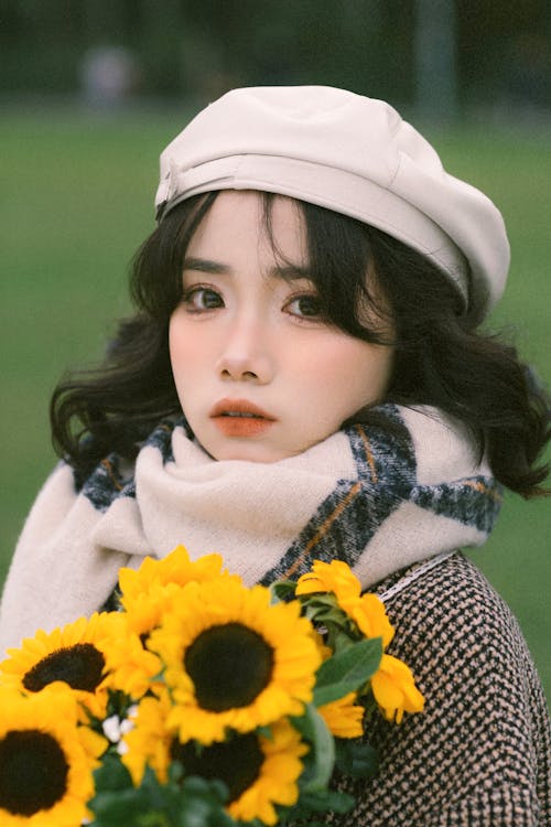A woman with a hat and scarf holding sunflowers