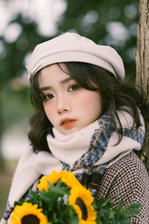 A girl with a hat and scarf holding sunflowers
