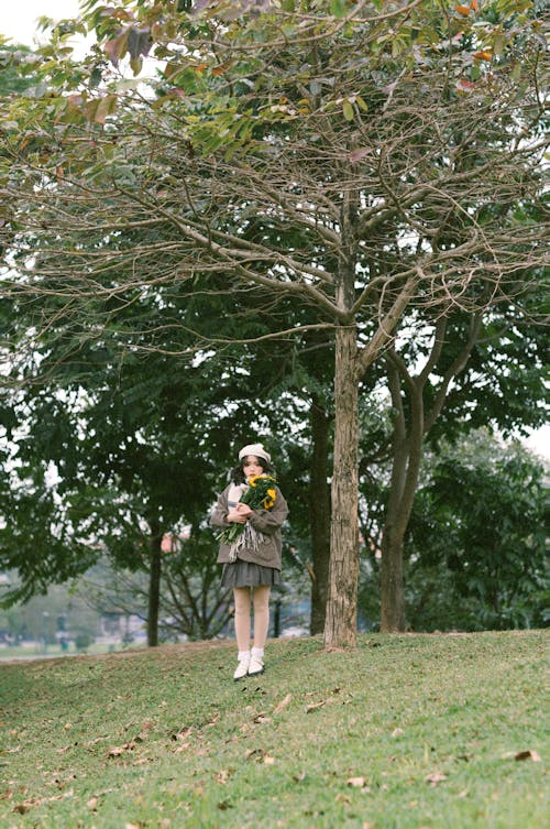 A woman is walking through a park with a yellow umbrella