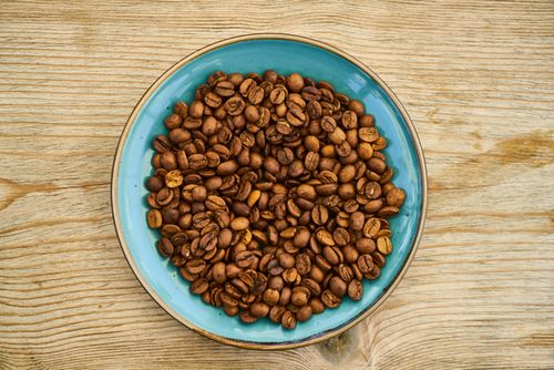 Free Top view of roasted coffee beans in a ceramic bowl on a wooden surface, perfect for coffee lovers. Stock Photo