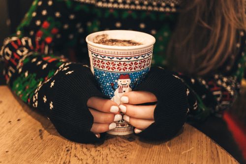 Free A woman in a sweater holds a decorated coffee cup indoors, capturing a cozy winter vibe. Stock Photo