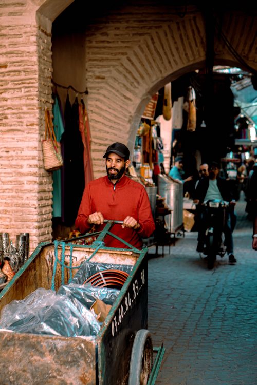 Free Man in red shirt pushing a cart through a bustling Moroccan bazaar street. Stock Photo