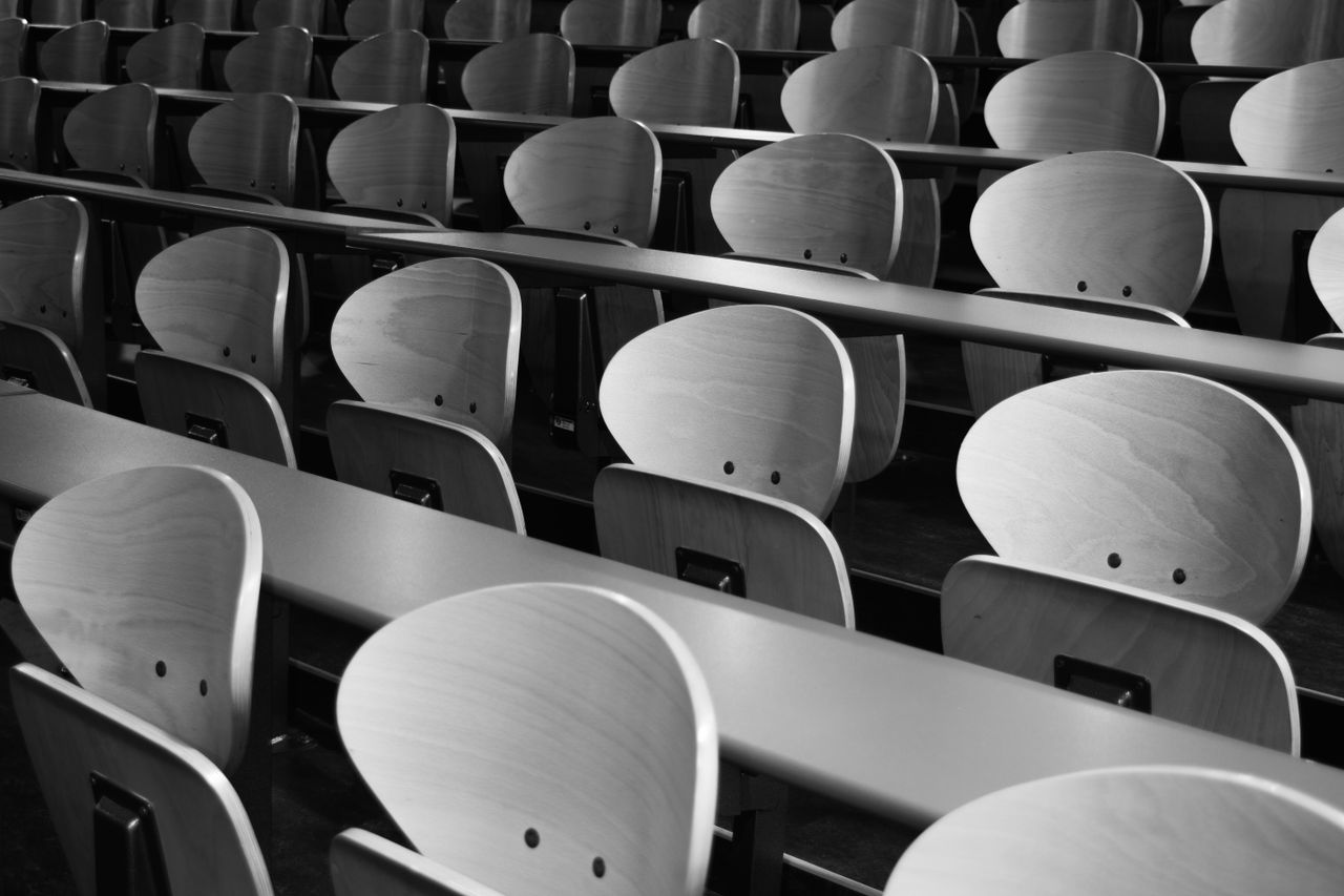 a monochrome view of empty wooden seats in a spacious lecture hall dis