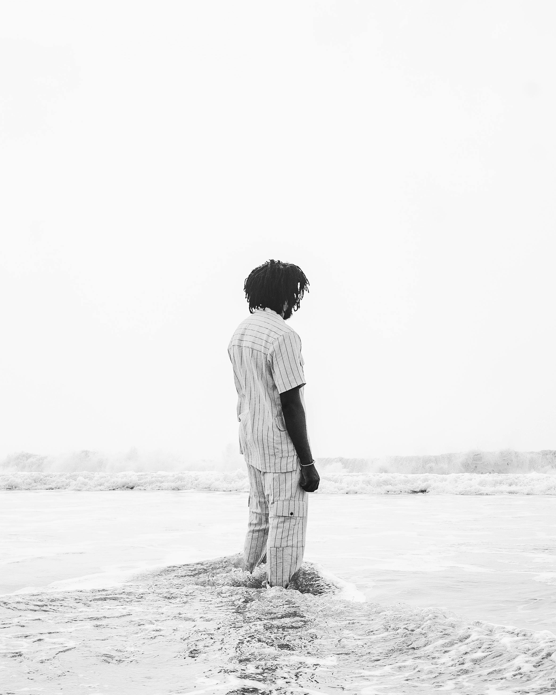 A serene black and white photograph of a man standing at the beach, evoking reflection and calmness.