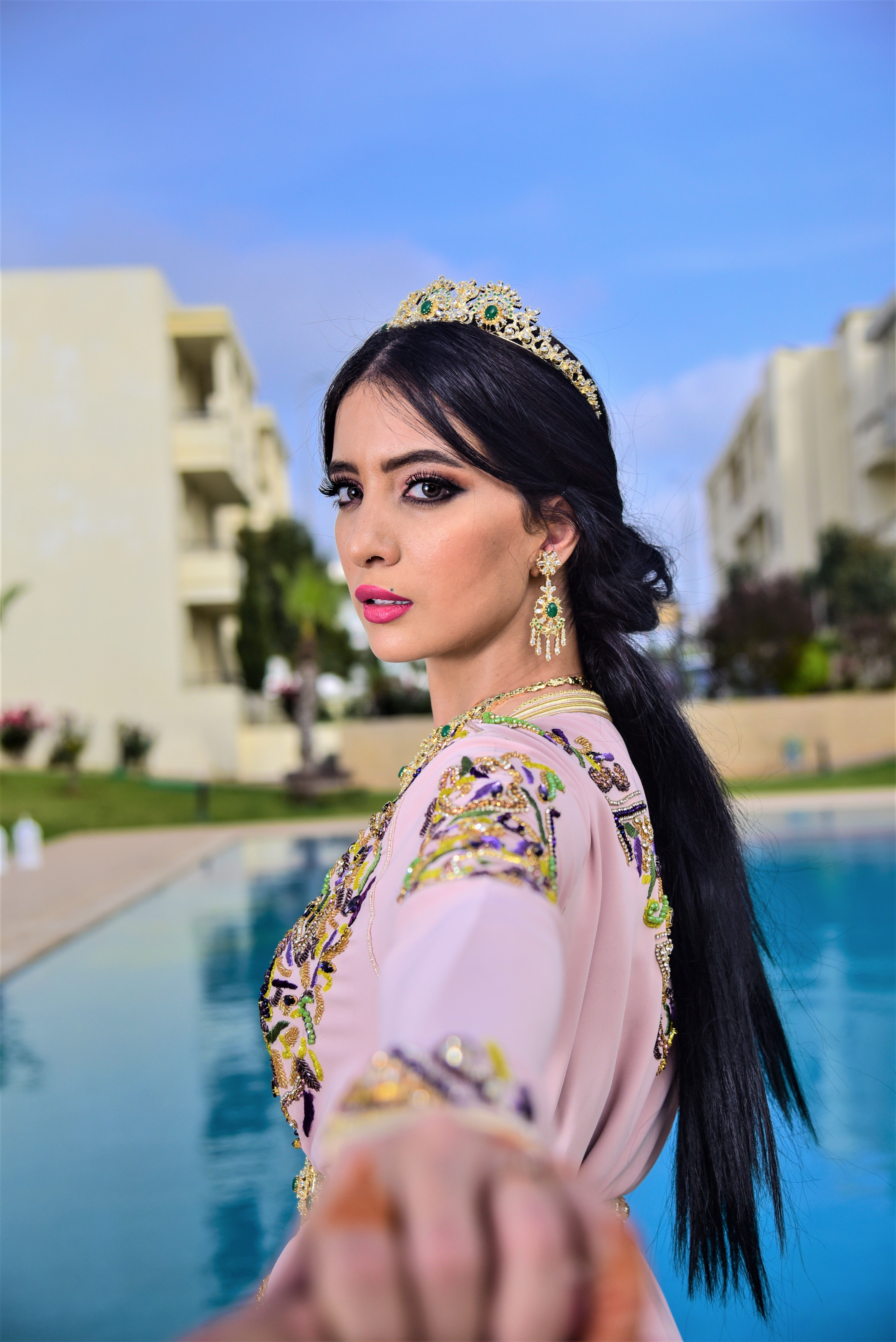 A woman in traditional attire with intricate jewelry by a pool, exuding elegance and charm.