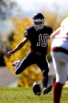 Action shot of a football player kicking the ball on a bright day in a stadium setting.