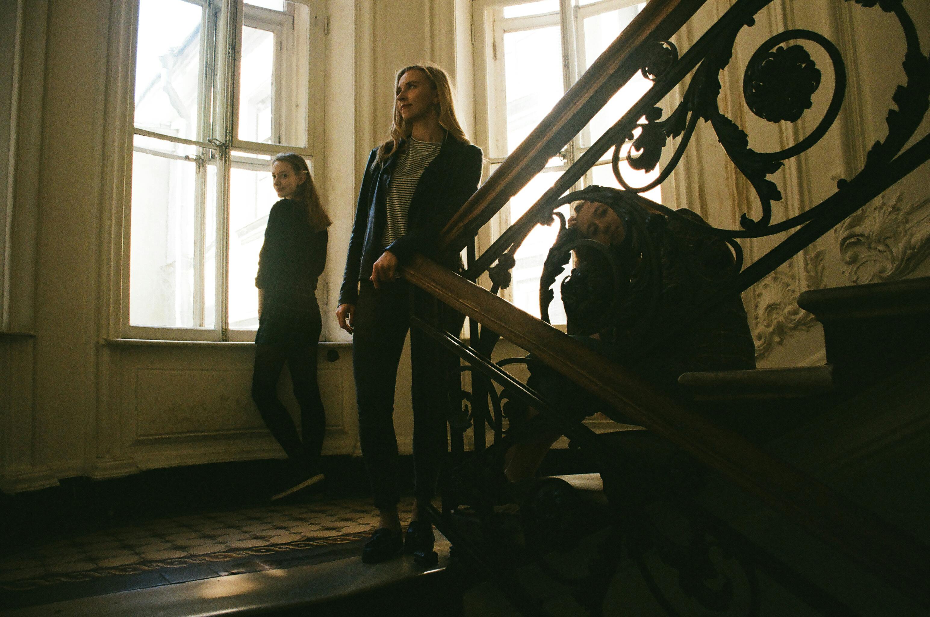 三位女士在华丽的室内楼梯上摆出姿势，营造出戏剧性且复古的氛围