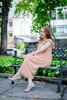 一位身着飘逸连衣裙的女子，正安坐在公园的长椅上，享受着宁静的时光