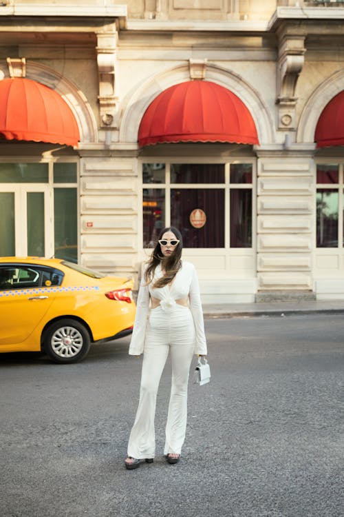 A woman in white pants and a white top standing in front of a yellow taxi