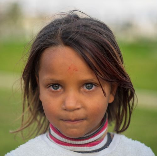 Free Close-up portrait of a young girl outdoors on a grassy field, looking directly at the camera. Stock Photo