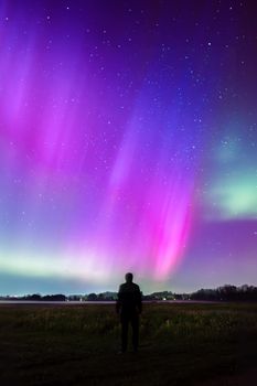 Silhouette of a man gazing at the colorful aurora borealis in a starry night sky.
