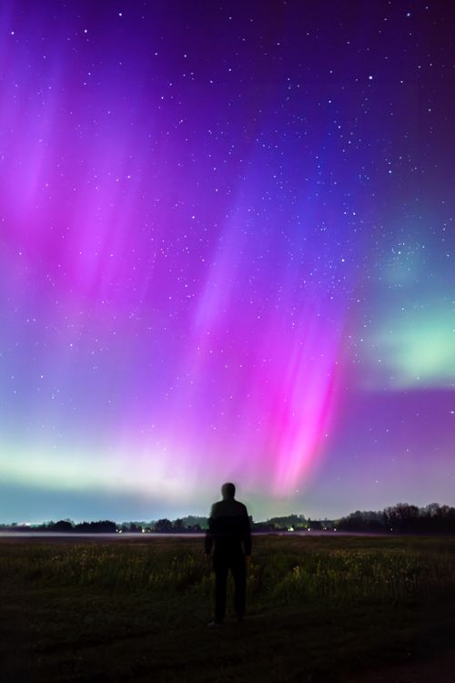 Free Silhouette of a man gazing at the colorful aurora borealis in a starry night sky. Stock Photo