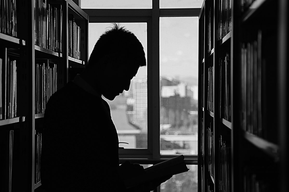 Moody silhouette of a person reading alone in a dim library, illustrative photo of quiet, isolated intellectual work