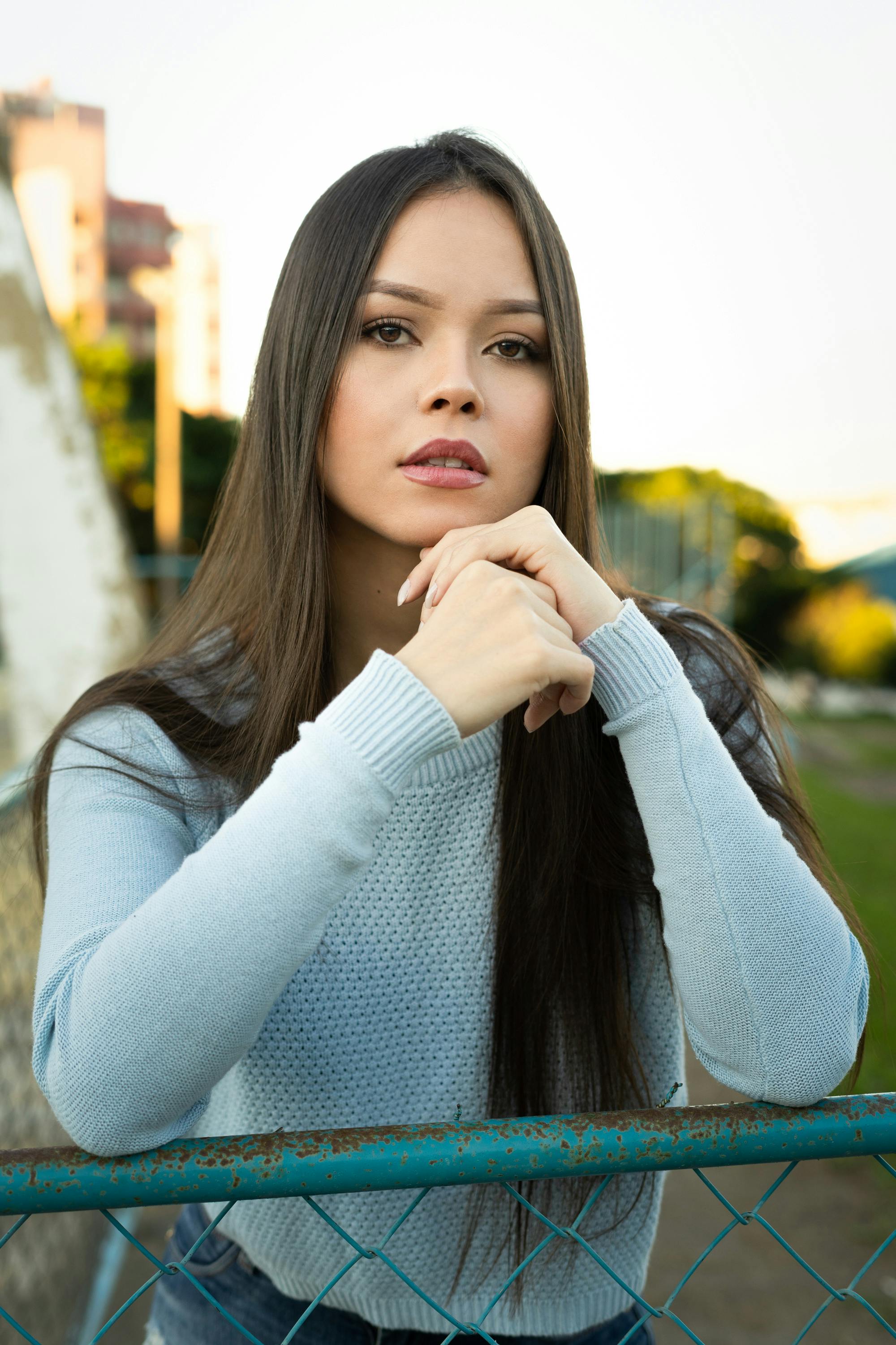 woman in teal sweater leaning on chain link fence