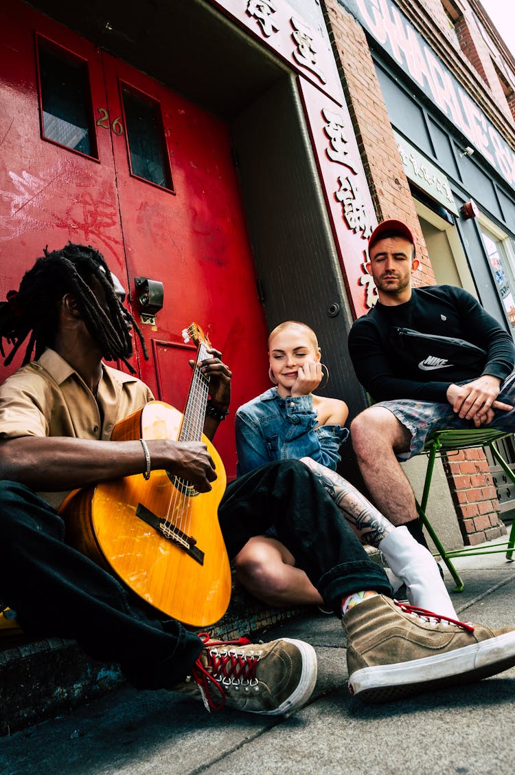 Man Playing Guitar Beside Woman And Man Listening To Him