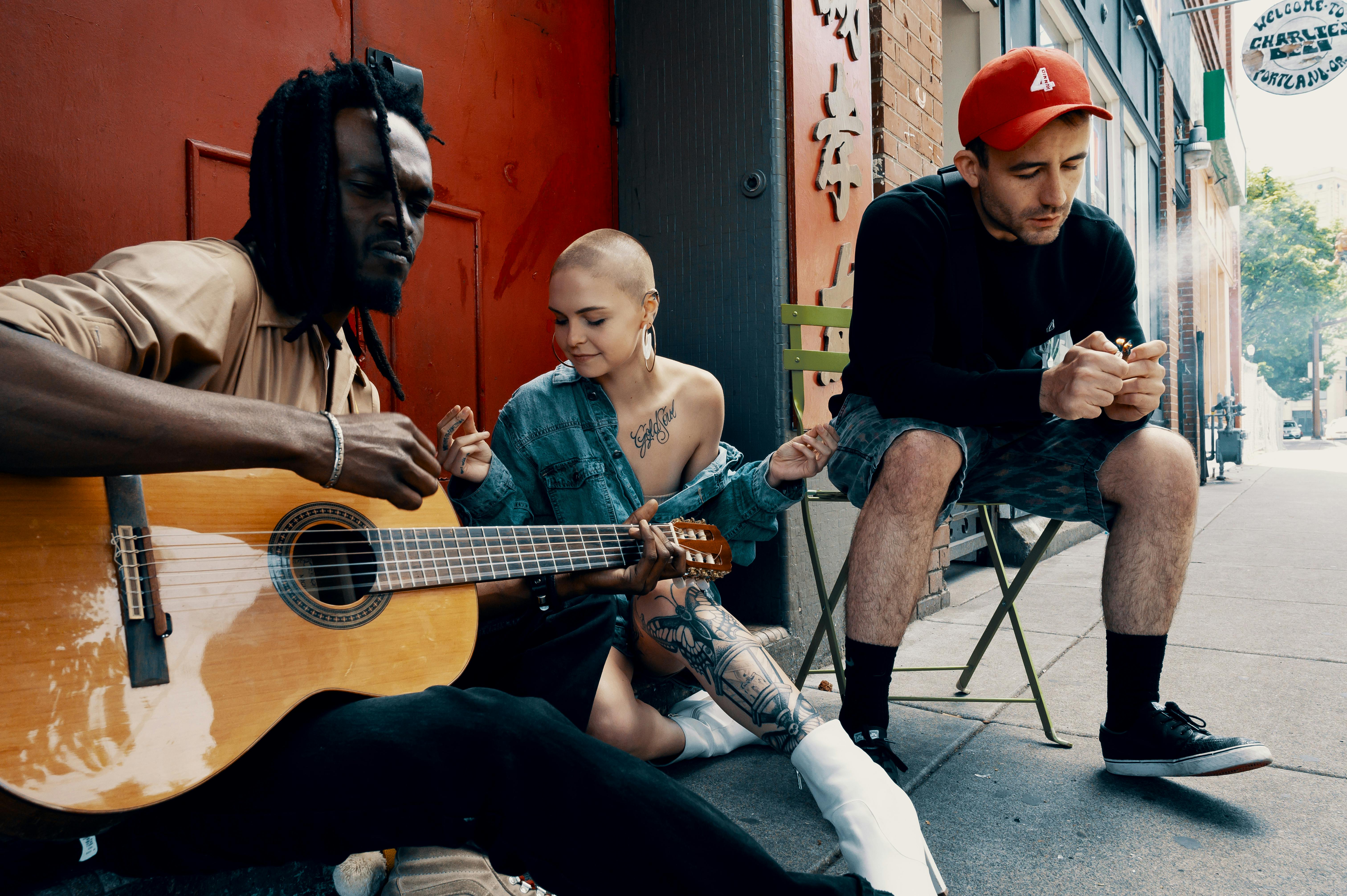 Diverse group of musicians playing guitar and relaxing on an urban street.