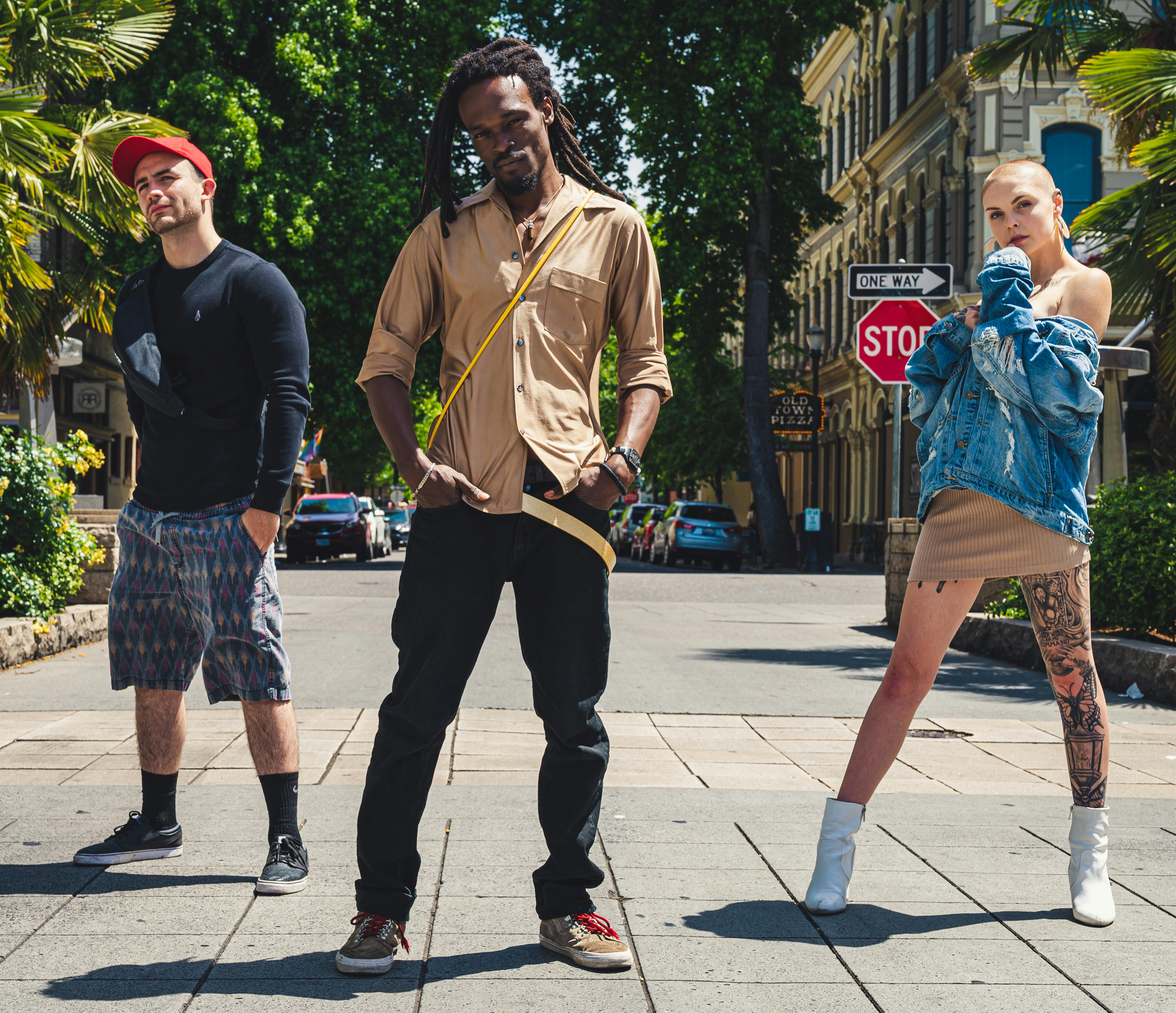 A diverse group of fashionable friends posing confidently outdoors under bright daylight in a city setting.