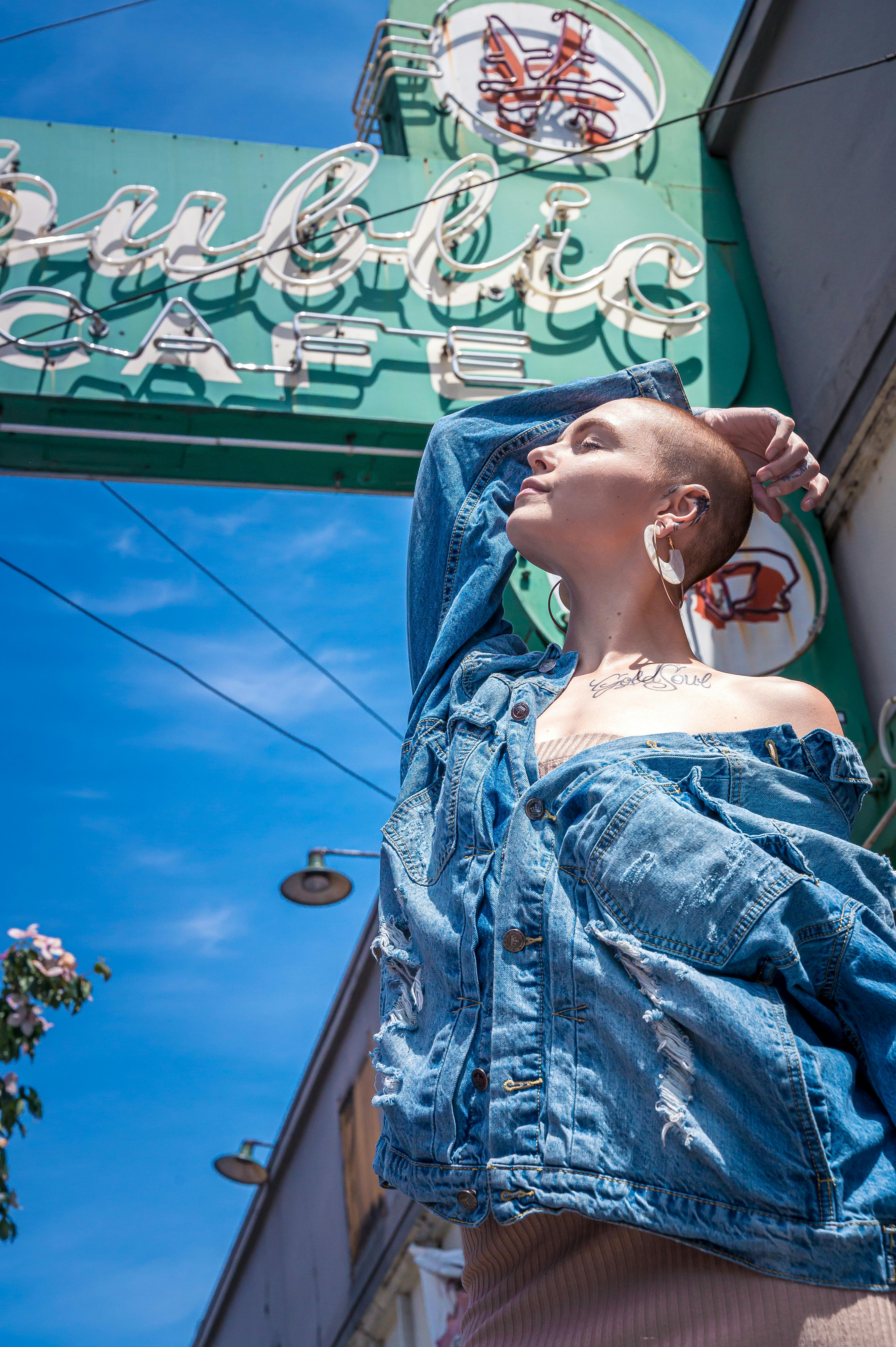 Fashionable woman enjoying the sun in front of a trendy city cafe. Denim jacket style.