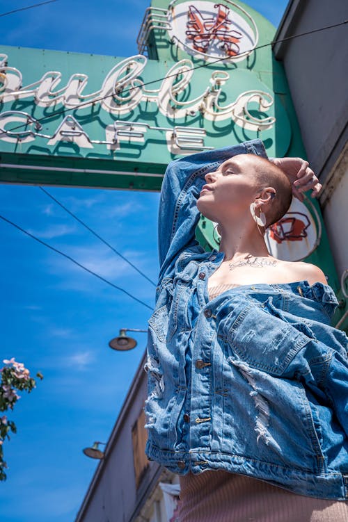 Foto De Baixo ângulo De Uma Mulher Com Uma Jaqueta Jeans Azul Posando Sob A Sinalização Do Café