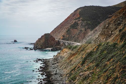 Free Captivating view of a coastal highway bridging rocky cliffs and the ocean. Stock Photo