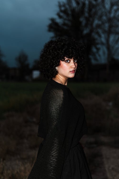 A woman with curly hair and black dress standing in the field